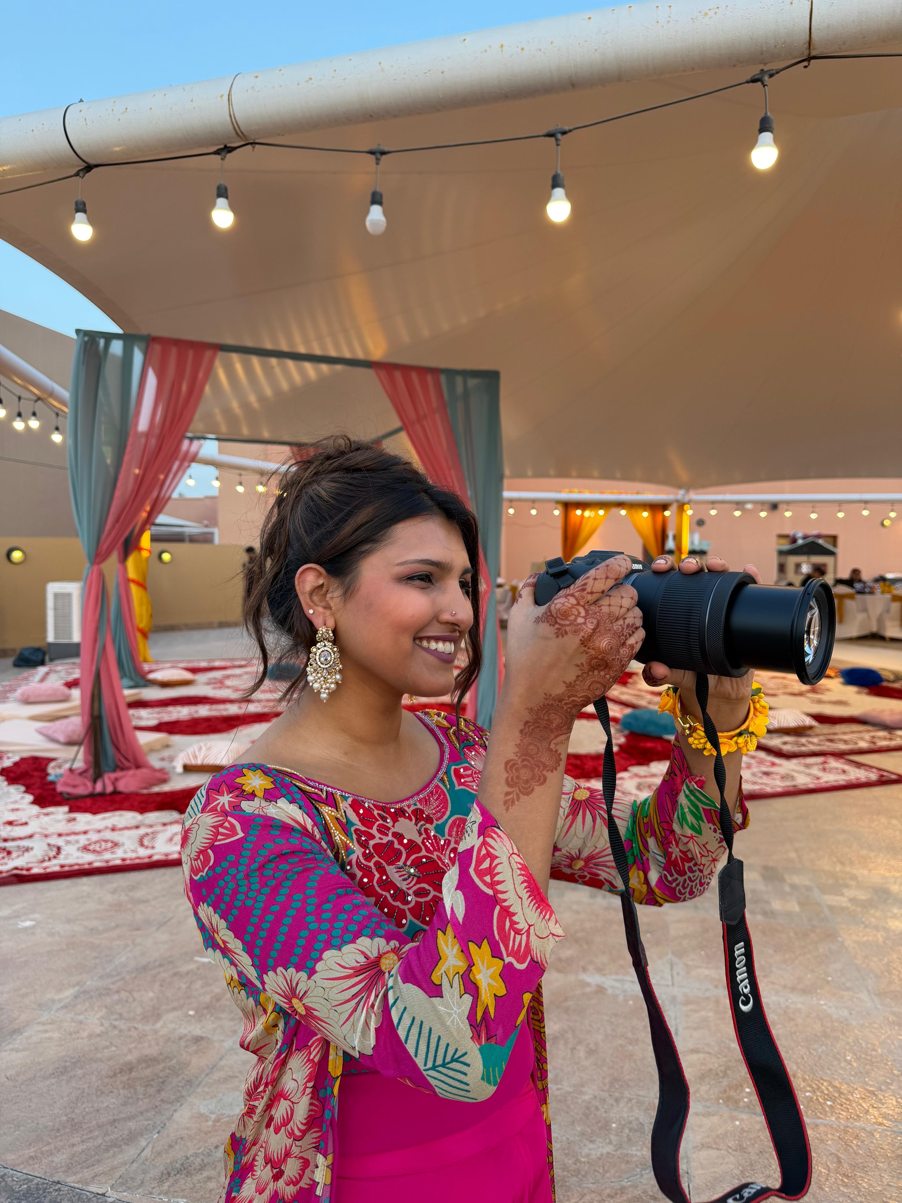 Sara holding a camera at a colorful South Asian wedding event