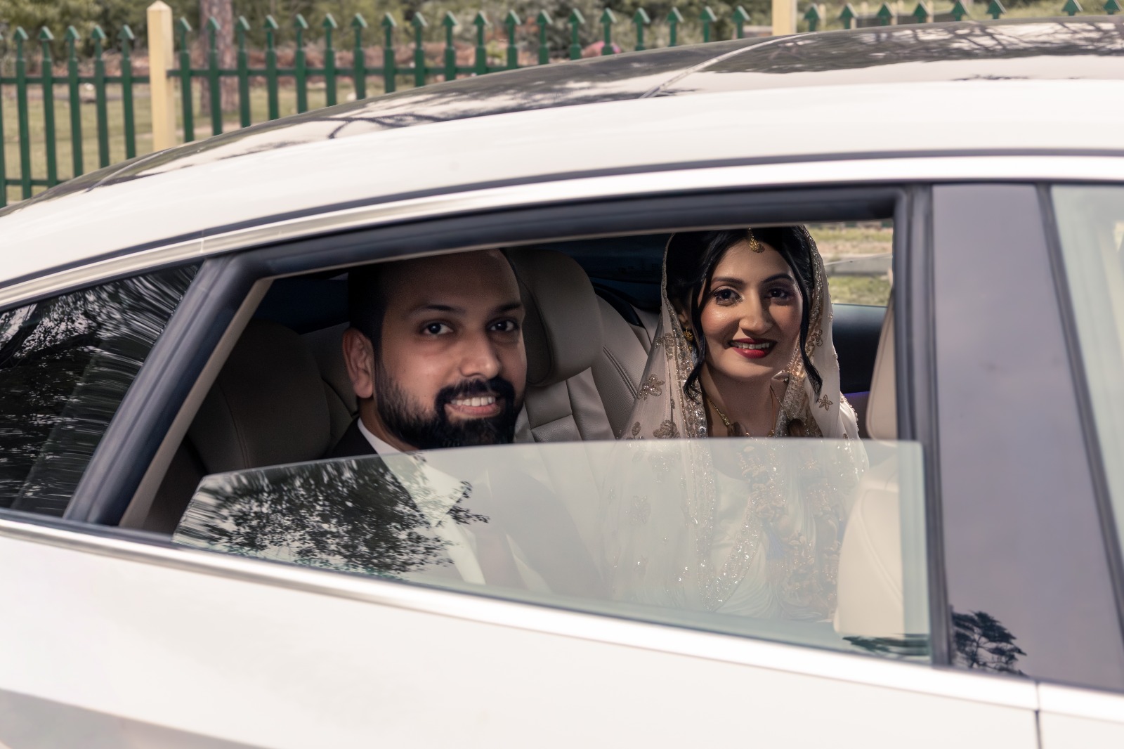 Bride and groom smiling through a car window